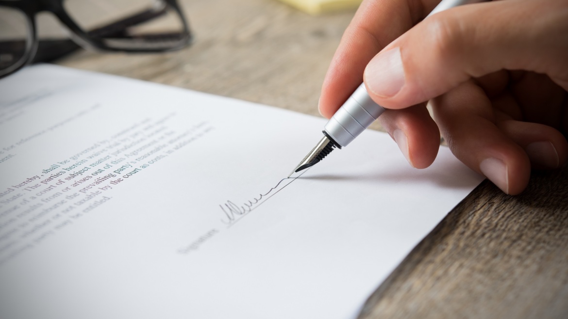 Close up of hand of businessman signing a form. Business man signing contract for future deal. Business man signing legal document. Male hand signing employee contract with a bond.